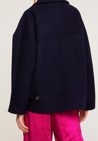 Veste en mélange de laine navy avec un large col, des coutures d'épaule et de grands boutons sur le devant. Le design présente une coupe décontractée et une texture lisse.