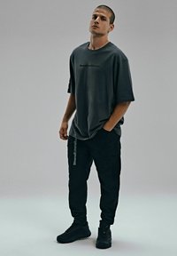 Przesadnie duża szara koszulka z nadrukowanym logo; zestawiona z czarnymi spodniami cargo z kieszeniami bocznymi i haftowanym akcentem. Czarne sneakersy.