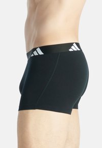 Fekete boxer alsónadrág, rugalmas anyagból, fekete derékpánttal, amelyen fehér Adidas logó és diszkrét varrási részletek találhatók.