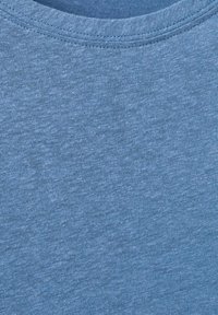 Gros plan sur un tissu en coton bleu doux avec un col rond, montrant la texture tricotée détaillée et les coutures.