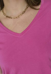 Roza V-neck majica od glatkog pamuka, s jednostavnim dizajnom i čistim šavovima, uparenim sa zlatnim lancem.