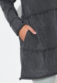 Dunkelgraues Langarm-Tunikakleid mit schichtweisem Design, rüschenbesetzten Kanten, Seitentasche und weichem, strukturiertem Stoff.