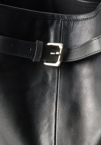 Prim-plan cu o curea neagră din piele, cu o cataramă metalică argintie, fixată în jurul unui material neted din piele neagră.