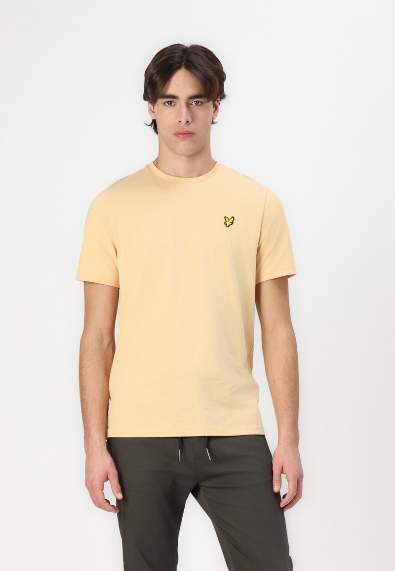 T-shirt jaune clair à manches courtes avec un col rond et un petit logo brodé vert sur la poitrine gauche. Fabriqué en tissu de coton doux.