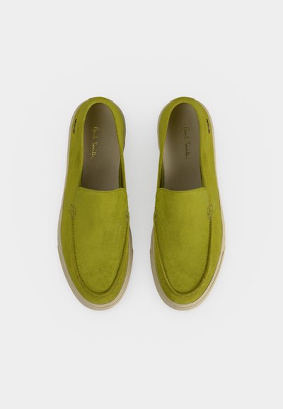 Ζευγάρι λαδιού πράσινα σουέντ παπούτσια χωρίς κορδόνια με μπεζ σόλες, από πάνω σε λευκό φόντο.