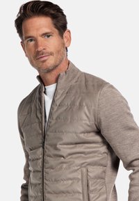 Beige gewatteerde bomberjack met textuur gebreide mouwen, opstaande kraag, volledige ritssluiting en zijzakken. Zacht, comfortabel materiaal.