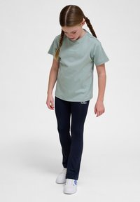 Jasnozielona bawełniana koszulka z krótkim rękawem i logo. Uzupełniona dopasowanymi granatowymi legginsami i białymi trampkami. Prosty, casualowy design.