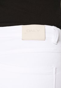 Jeans de ganga brancos com uma textura suave, apresentando um etiqueta de couro rotulada "ONLY". Inclui passantes para cinto e detalhes de costura.