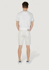 Camisa polo blanca con ribetes grises, combinada con pantalones cortos blancos. La parte trasera muestra detalles del logo en la camiseta y bolsillos traseros en los pantalones cortos. Zapatillas blancas.