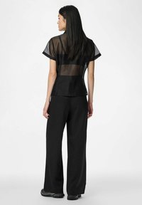 Top noir transparent à manches courtes, coupe ajustée, associé à un pantalon large à rayures fines noir. Matériau notablement transparent.