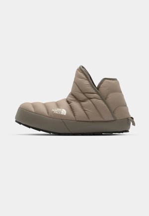 Polstret beige slip-on sko med en struktureret overdel, lukket bag og gummisåler med en lille træksløjfe ved hælen.