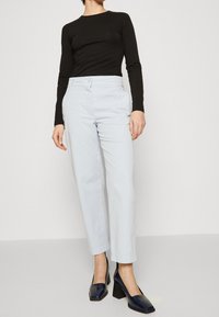 Ljusblå byxor med hög midja och avslappnad passform, kombinerat med en svart långärmad topp och marinblå blockklackskor med fyrkantig tå.