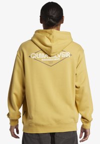 Yellow hoodie with a large white Quiksilver logo on the back. Made of soft fabric, featuring a kangaroo pocket and elastic cuffs.