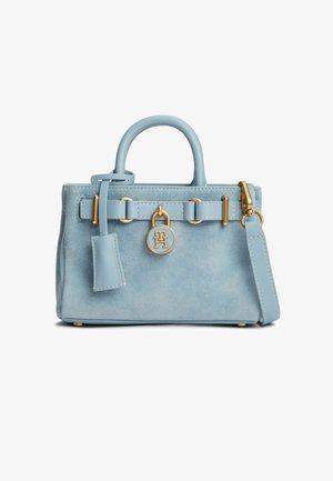 Lichtblauwe suède handtas met handgreep aan de bovenkant, afneembare band, goudkleurige hardware en een ronde gouden logo-bedel aan de voorkant in het midden.