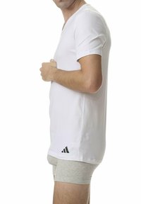 Vit t-shirt med V-ringning i bomull, med korta ärmar och en svart Adidas-logga på vänster sida, tillsammans med grå kalsonger.