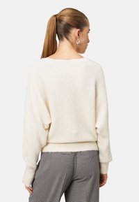 Miękki sweter w kremowym kolorze o luźnym kroju, z prążkowanym wykończeniem i rękawami w kształcie balonów, połączony z wzorzystymi, dopasowanymi spodniami. Elegancki i przytulny design.