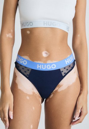 Marineblauwe ondergoed met een lichtblauwe elastische tailleband met het "HUGO" logo, doorschijnende polka dot mesh zijkanten en een gladde textuur.