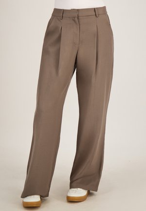 Bruine wijde broek met hoge taille, plooien, riemlussen en een verborgen voorzijde, gedragen met witte sneakers.