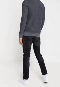 Sudadera gris oscura con dobladillo y puños acanalados, combinada con jeans ajustados negros y zapatillas blancas, vista desde atrás.