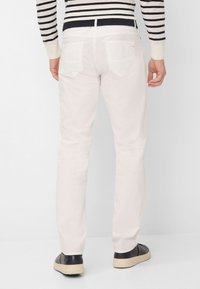 Witte slim-fit broek met een gladde textuur, voorzien van twee achterzakken en een lage taille, gecombineerd met zwarte sneakers en een gestreepte trui.