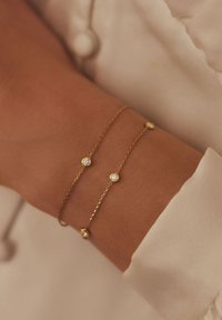 Gold chain bracelet featuring two strands with small, round, clear gemstones evenly spaced along the length. Textured links enhance the design.