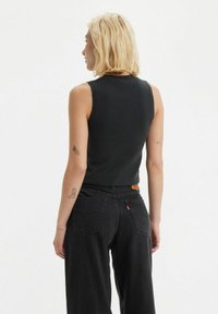 Svart ärmlös topp med en smal passform, tillverkad av ribbat tyg. Bärs tillsammans med högmidjade svarta jeans med en läderetikett och sidofickor.