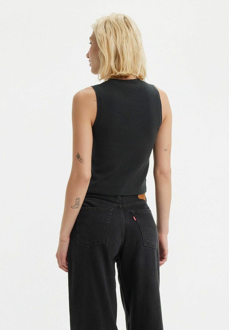 Top negro sin mangas con un diseño ajustado, hecho de tela acanalada. Combinado con jeans negros de cintura alta con una etiqueta de piel y bolsillos laterales.