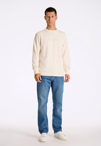 Ljusbeige sweatshirt med rund halsringning och präglad text "COPENHAGEN", matchad med blå denimjeans och vita sneakers.