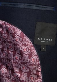 Veste bleu marine foncé avec doublure bordeaux à motif paisley et une étiquette noire indiquant "Ted Baker London" taille 2 à l'intérieur du col.