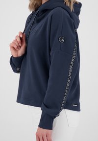 Sudadera con capucha de color azul marino, de corte relajado, con capucha ajustable, puños acanalados y detalles de logo a lo largo de la manga.