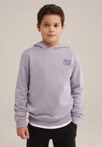 Fialová mikina s predným vreckom typu kengura, rebrovanými manžetami a spodným lemom. Obsahuje textúrovanú nášivku na ľavej strane hrude. Skombinovaná s čiernymi nohavicami.