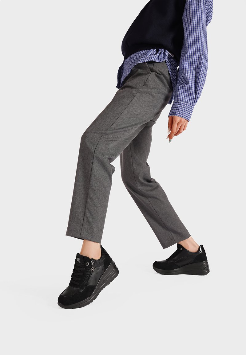 Sneakers neri con dettagli in suede texture e pelle liscia, dotati di lacci e cerniera laterale. Indossati con pantaloni grigi su misura e camicia blu.