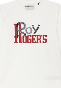 T-shirt bianco in cotone con un design grafico. Il testo "Roy Roger's" in rosso e argento, con un motivo della cintura integrato nelle lettere.