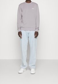Felpa grigia chiara con polsini e scollatura a costine, con un piccolo logo bianco. Abbinate a jeans azzurri e sneakers bianche.