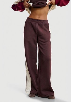 Bordowe spodnie dresowe z kremowymi panelami po bokach, elastycznym paskiem i rozszerzanymi nogawkami. Wykonane z miękkiego, elastycznego materiału dla komfortu.