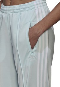 Lichtblauwe sportbroeken met een ritszak, voorzien van witte drie-streep accenten en een geborduurd logo op het onderbeen.