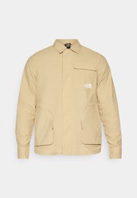 Jasnobeżowa kurtka z kołnierzem na guziki, kieszenią na piersi oraz dwoma dużymi kieszeniami po bokach. Wykonana z gładkiej tkaniny o luźnym kroju.