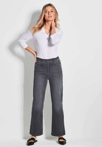 Dunkelgraue Jeanshose mit weitem Bein, ausgestattet mit einem elastischen Bund und Fronttaschen, kombiniert mit einem weißen Langarmoberteil.