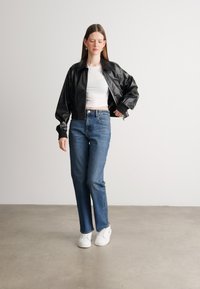 Jachetă bomber neagră din piele, bluză albă ajustată, blugi drepti albastre, adidași albi; textură netedă, croială lejeră, contrast de culori.