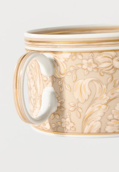 Porcelain cup with ornate gold and beige floral patterns and a curved white handle with gold trim.
