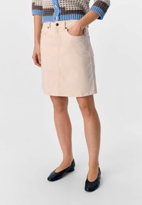 Jupe en denim beige avec une coupe droite, poches avant et couture contrastante. Portée avec des chaussures plates noires et un cardigan en tricot multicolore.