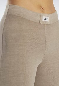 Béžové legíny vyrobené z mäkkej, elastickej tkaniny s priliehavým strihom. Obsahujú široký elastický pás s logom na prednej strane.