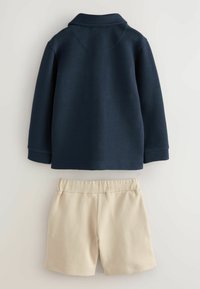 Marineblauwe textuurjack met een kraag, gecombineerd met lichtbeige shorts met een elastische tailleband. Gladde stof en casual ontwerp.
