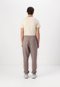 Beige shirt met korte mouwen en ruime, lichtbruine joggingbroek met elastische tailleband en twee achterzakken, gedragen met witte sneakers.
