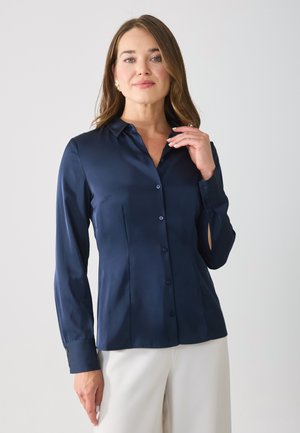 Navy blue, satin button-up shirt with long sleeves, collar, and subtle side slits. Features a smooth texture and seven front buttons.