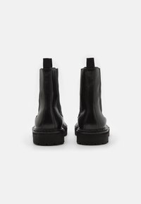 Černé kožené kotníkové boty s elastickými bočními panely, plochými gumovými podrážkami a poutky na zadní straně, s hladkým povrchem a minimálním prošíváním.