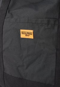 Μαύρη καμβά τσάντα με υφή και ορατή πορτοκαλί ετικέτα που αναγράφει "Service Works." Διαθέτει μπροστινή τσέπη για αποθήκευση.