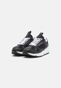 Black and white athletic shoes featuring a mix of smooth leather and mesh, with a chunky sole and prominent lacing. Logo on the tongue.