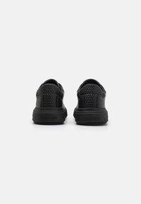 Černé tenisky se tkanou texturou na svršku, s kulatou špičkou, plochou podrážkou a jemným logem na patě.