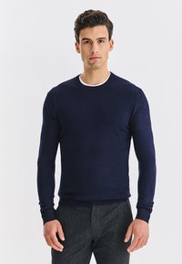 Granatowy, dziergany sweter z okrągłym dekoltem, długimi rękawami i pr�ążkowanymi mankietami. Gładki, lekki materiał o dopasowanej sylwetce.